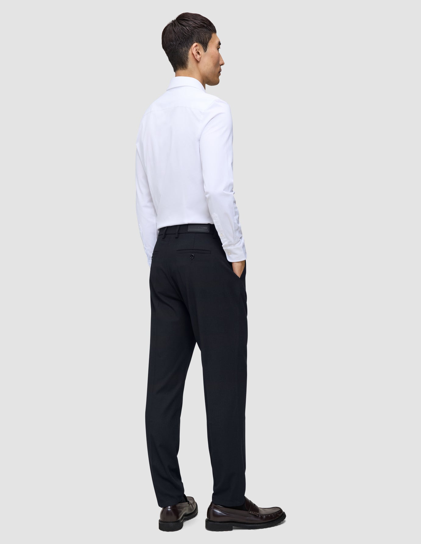 En mann i hvit skjorte og en Midnight Blue Motion Suit Pants Regular-bukse står med ryggen til kameraet.